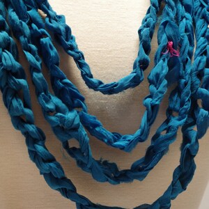 May include: A blue crocheted necklace made from fabric strips. The necklace is layered and has a braided design.