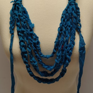 May include: A teal blue crocheted necklace made from fabric strips. The necklace is layered and has a long, flowing design.