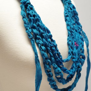 May include: A turquoise blue fabric necklace with multiple strands woven together. The necklace is displayed on a white mannequin.