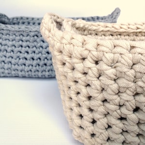 May include: Two crocheted baskets, one in a light gray color and the other in a cream color. The baskets are made with a thick yarn and have a simple, classic design.