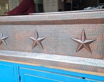 May include: A copper farmhouse sink with a hammered finish and three star-shaped cutouts. The sink is a rectangular shape and has a slightly raised edge.