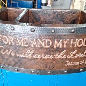 May include: A copper farmhouse sink with two basins and a hammered finish. The sink has a black metal rim with rivets and a personalized inscription: "As for me and my house, we will serve the Lord." Joshua 24:15