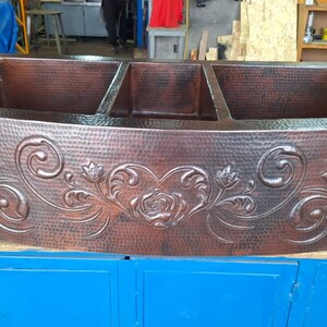May include: A large, three-basin copper kitchen sink with a hammered finish and an ornate floral design. The sink is made of solid copper and has a beautiful, rustic look.