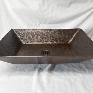 May include: A rectangular copper sink with a hammered finish. The sink has a square drain in the center.