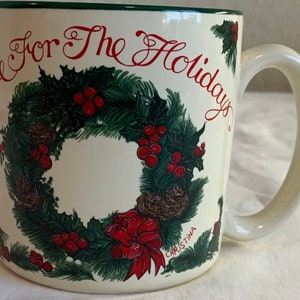 Peut inclure: Une tasse en céramique blanche avec un motif de couronne de Noël verte et rouge. La tasse a une anse et dit "Time For The Holidays" en lettres rouges.