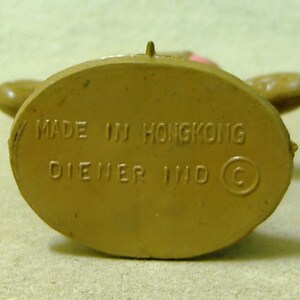 May include: Close-up of the bottom of a brown plastic toy figure. The bottom is marked with the text "MADE IN HONGKONG DIENER IND C".