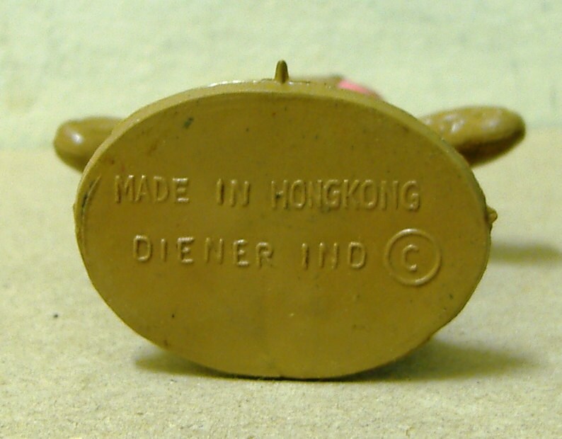 May include: Close-up of the bottom of a brown plastic toy figure. The bottom is marked with the text "MADE IN HONGKONG DIENER IND C".