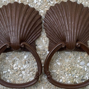 May include: Two brown seashell-shaped door handles with a ring pull. The handles are made of metal and have a smooth, polished finish.