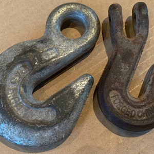 May include: Two metal hooks, one silver and one rusty brown. The silver hook has a round opening at the top and the words "Grade 80" stamped on the side. The rusty brown hook has the words "Forged China" stamped on the side.