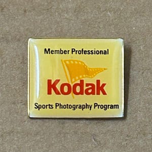 Könnte beinhalten: Ein gelber und roter Kodak-Pin mit dem Text "Member Professional Kodak Sports Photography Program".