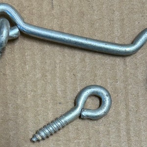 Puede incluir: Dos cierres de gancho y ojo de metal plateado con tornillos. Los cierres de gancho y ojo se utilizan para asegurar puertas, portales u otros objetos.
