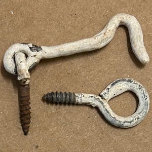 Peut inclure: Deux loquets anciens en métal blanc, un crochet et un œillet. L'un a un crochet incurvé et une vis. L'autre a un œillet à vis. Le métal a un aspect vieilli et usé avec de la rouille.