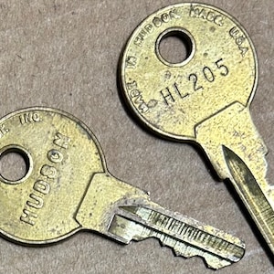 Puede incluir: Dos llaves de latón, una con el texto "HUDSON LOCK INC." y la otra con el texto "MADE IN RHODE ISLAND USA HL205".