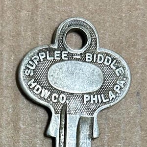 Könnte beinhalten: Ein silberfarbener Schlüssel mit einem herzförmigen Kopf. Der Kopf ist mit dem Text "SUPPLEE - BIDDLE - HDW. CO. - PHILA. PA." graviert.