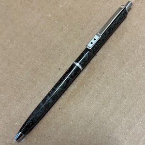 Op de afbeelding: Een zwarte en zilveren pen met een marmerpatroon. De pen heeft een zilveren clip en een zilveren band met drie zwarte hartjes.