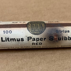 May include: A glass tube containing 100 red litmus paper strips. The label reads "Litmus Paper Squibb RED" and "Responds to N/250 alkali volumetric solution".