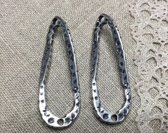 May include: Two silver oval-shaped earrings with a textured surface. The earrings have a hammered metal look and are designed with a simple, minimalist style.
