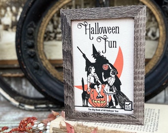 May include: A framed vintage Halloween print with the words "Halloween Fun" in a decorative font. The image features a witch, children, a black cat, and a jack-o'-lantern. The frame is a rustic gray color.