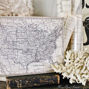 May include: An antique map of the United States, displayed with a vintage book and a piece of white coral. The map is framed and shows the states in detail. The words "United States" are visible.