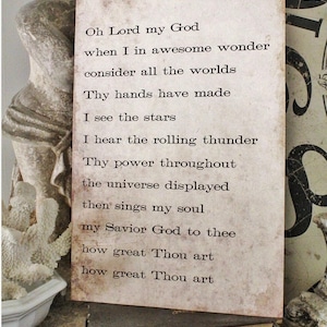 May include: A rectangular, vintage-style sign with the text of a religious poem printed in black. The sign has a distressed, aged appearance with a light brown background. The sign is propped up on a stack of old books.