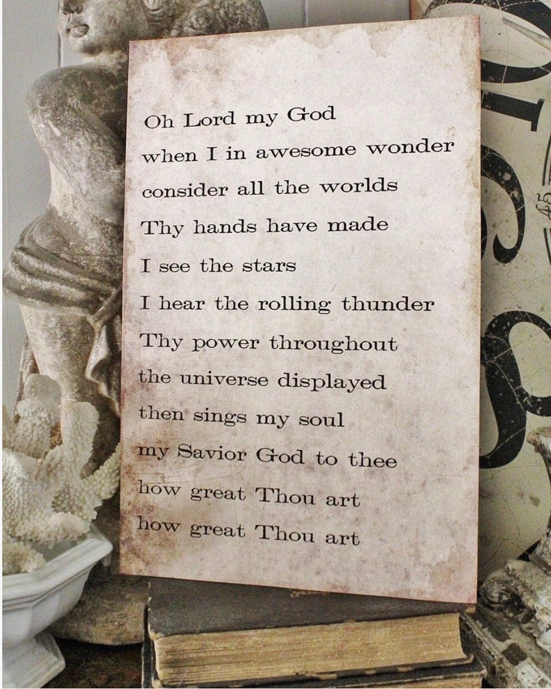 May include: A rectangular, vintage-style sign with the text of a religious poem printed in black. The sign has a distressed, aged appearance with a light brown background. The sign is propped up on a stack of old books.