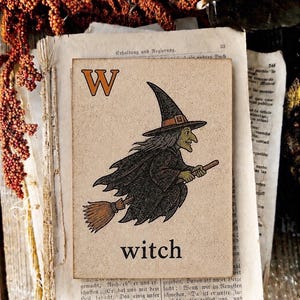 Puede incluir: Una placa rectangular de madera con una ilustraci&oacute;n impresa de una bruja con sombrero puntiagudo y capa negra volando sobre una escoba. La letra W est&aacute; en la esquina superior izquierda y la palabra witch est&aacute; impresa en negro abajo al centro.