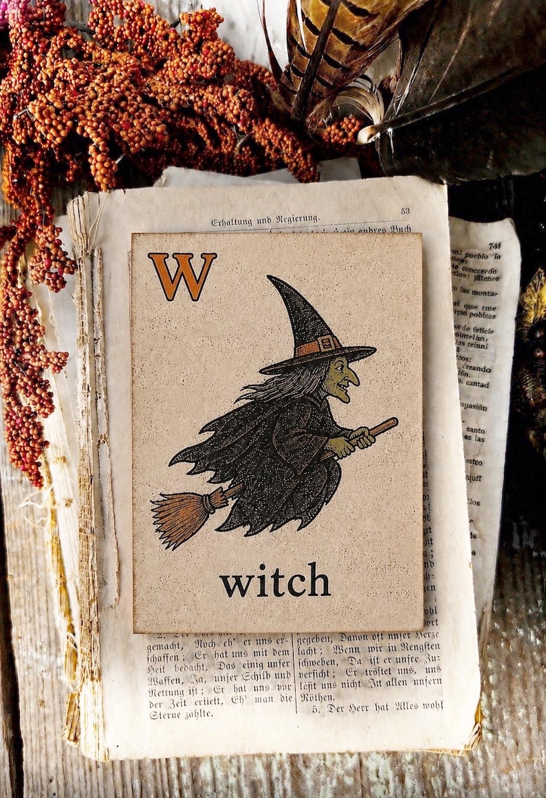 Puede incluir: Una placa rectangular de madera con una ilustraci&oacute;n impresa de una bruja con sombrero puntiagudo y capa negra volando sobre una escoba. La letra W est&aacute; en la esquina superior izquierda y la palabra witch est&aacute; impresa en negro abajo al centro.