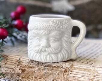 Taza pequeña vintage de loza de Papá Noel blanca con decoración navideña de estilo rústico.