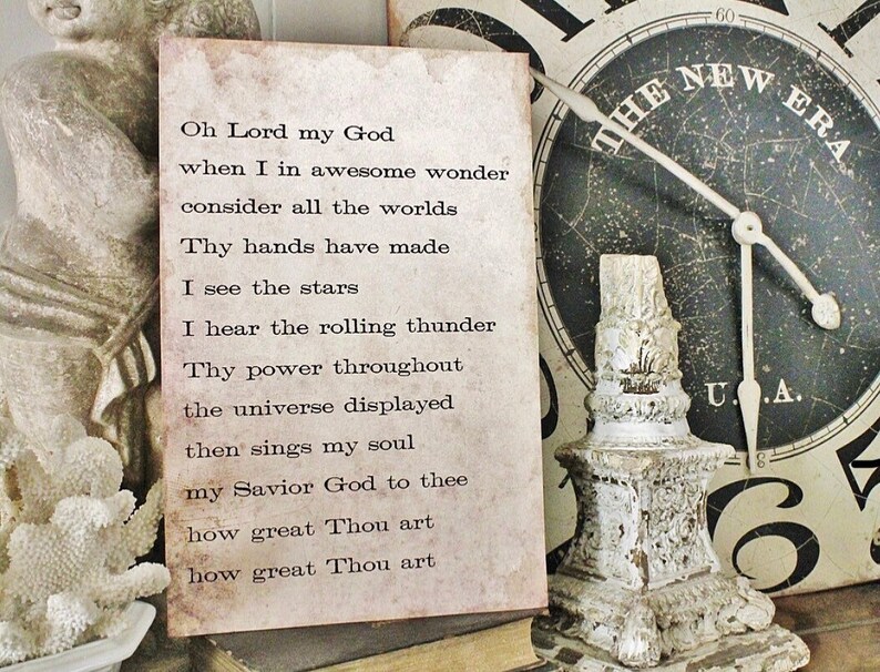 May include: A vintage-style print with the text of a hymn, "Oh Lord my God." The print has a distressed, aged appearance with brown and beige tones. A decorative, white, ornate candle holder and a clock with the text "The New Era" are in the background.