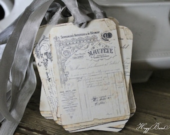 May include: A stack of vintage-style paper tags with gray ribbon. The tags feature faded black text and illustrations, with the word "MAUFEVE" prominently displayed. The tags have a distressed, aged appearance, suggesting they are antique or handcrafted.