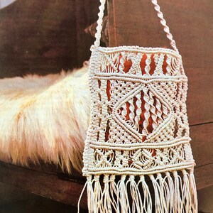 Może przedstawiać: Biała torebka z makramą z frędzlami na dole. Torebka wisi na drewnianym krześle.