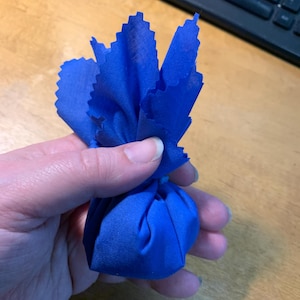 May include: A blue cloth bag tied at the top, held in a hand.