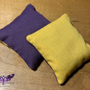 May include: Two fabric bean bags, one purple and one yellow. The bean bags are made of a soft, textured fabric and are perfect for playing games or relaxing.