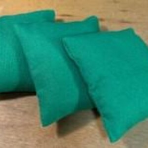 May include: Three green bean bags are arranged on a wooden surface. The bean bags are rectangular and appear to be made of a textured fabric. The bean bags are a vibrant shade of green.