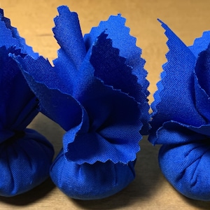 May include: Three blue fabric pouches tied with a knot at the top. The pouches are arranged in a row on a wooden surface.