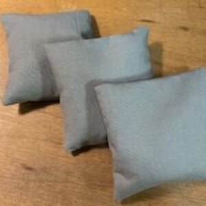 May include: Three square, light gray throw pillows arranged on a wooden surface. The pillows are made of a soft fabric and appear to be filled with a lightweight material. Each pillow is approximately 10 inches square.