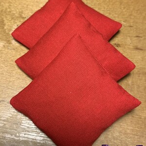 May include: Three red fabric bean bags stacked on top of each other. The bean bags are square shaped and have a textured surface.