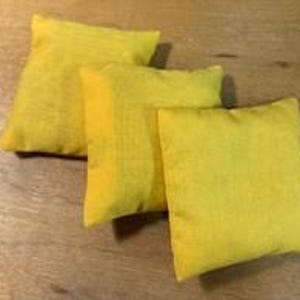 May include: Three square, yellow throw pillows arranged on a wooden surface. The pillows have a textured appearance and are filled with a soft material. Each pillow measures approximately 12 inches square.