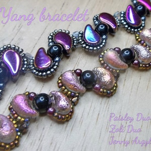 Könnte beinhalten: Nahaufnahme von zwei Armbändern mit Perlen. Die Armbänder haben schillernde tropfenförmige Perlen in Lila und Blau sowie schwarze Perlen und paisleyförmige Perlen in Rosa- und Goldtönen. Der Text "Yin Yang bracelet" ist sichtbar.