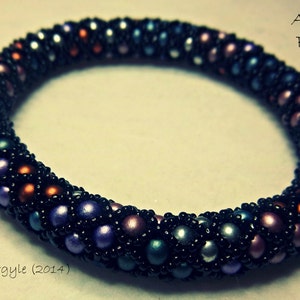 Op de afbeelding: Argyle armband met kralen. De armband heeft een donkere achtergrond met kleurrijke kralen in tinten paars, oranje, groen en zilver. De tekst "Argyle Bangle" en "Jenny Argyle (2014)" zijn zichtbaar.