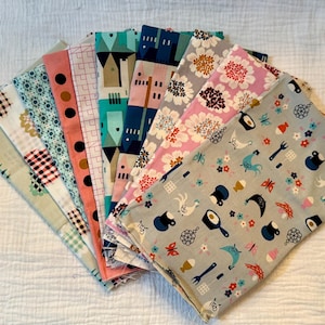 May include: A collection of colorful fabric swatches arranged in a fan shape. The fabrics feature various patterns, including floral, geometric, and novelty prints. Colors include pink, blue, green, and black.