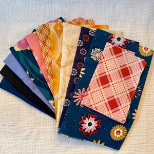 May include: A collection of fabric swatches in various colors and patterns, including floral, geometric, and plaid designs. The fabrics are arranged in a fan shape, showcasing a range of textures and hues, from deep blues to vibrant oranges and pinks.