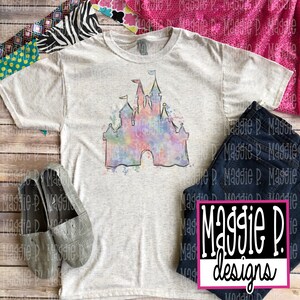 May include: A light gray t-shirt with a watercolor-style illustration of a castle in pink, blue, and yellow hues. The castle is outlined in black and has a white background.