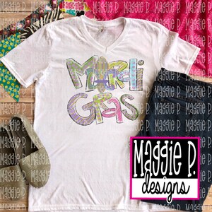 May include: White t-shirt with a colorful "Mardi Gras" design. The shirt has a V-neck and short sleeves. The design is in a cartoon style with purple, green, yellow, and pink colors.