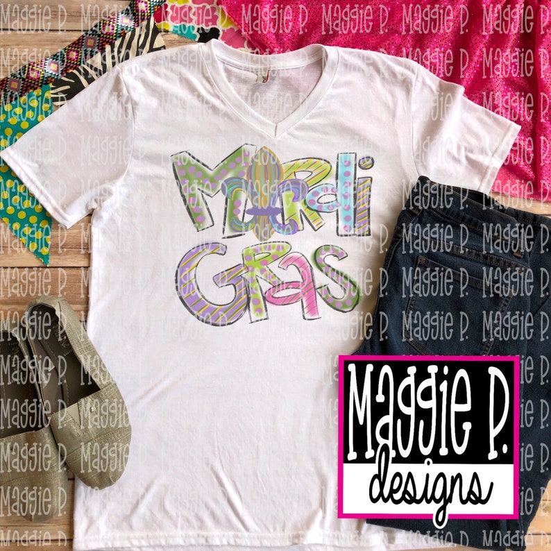 May include: White t-shirt with a colorful "Mardi Gras" design. The shirt has a V-neck and short sleeves. The design is in a cartoon style with purple, green, yellow, and pink colors.