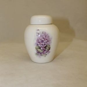 May include: White ceramic jar with a lid and a floral design featuring purple flowers and green leaves.