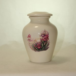 May include: A white ceramic urn with a floral design featuring pink and purple irises. The urn has a lid and is approximately 6 inches tall.