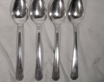 May include: Four silver spoons with ornate designs on the handles. The spoons are arranged in a row, with the handles pointing to the right.