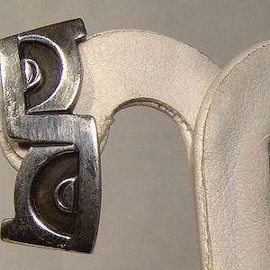 May include: A pair of silver earrings with a geometric design. The earrings are made of two pieces that are connected by a hinge. The earrings are in the shape of a circle with a smaller circle inside of it.