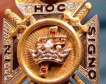 May include: A gold-toned pendant with a black enamel cross and a crown. The pendant features the words "HOC SIGNO VINCES" in black lettering.